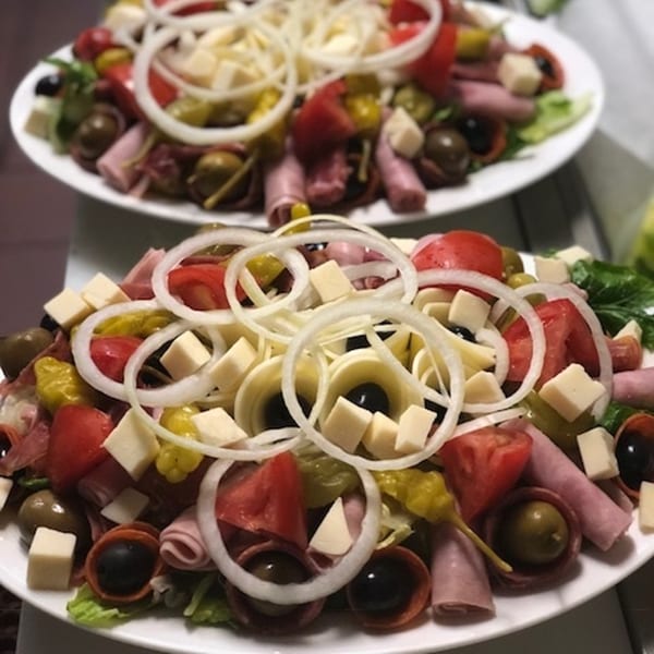 Two large Italian antipasto salads with meats, cheeses, olives, tomatoes, and onions on white plates.