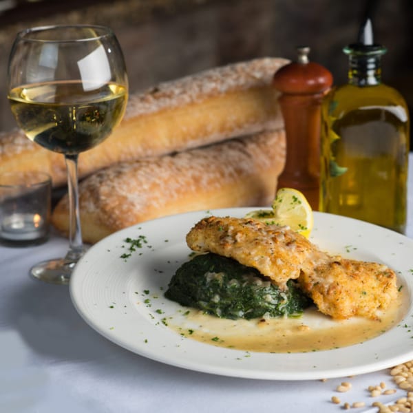 Zuccarelli's Italian Restaurant's breaded fish with spinach, white wine, and baguettes on a table.