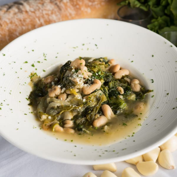 A white bowl of Zuccarelli's Italian greens and beans, garnished with cheese and parsley.